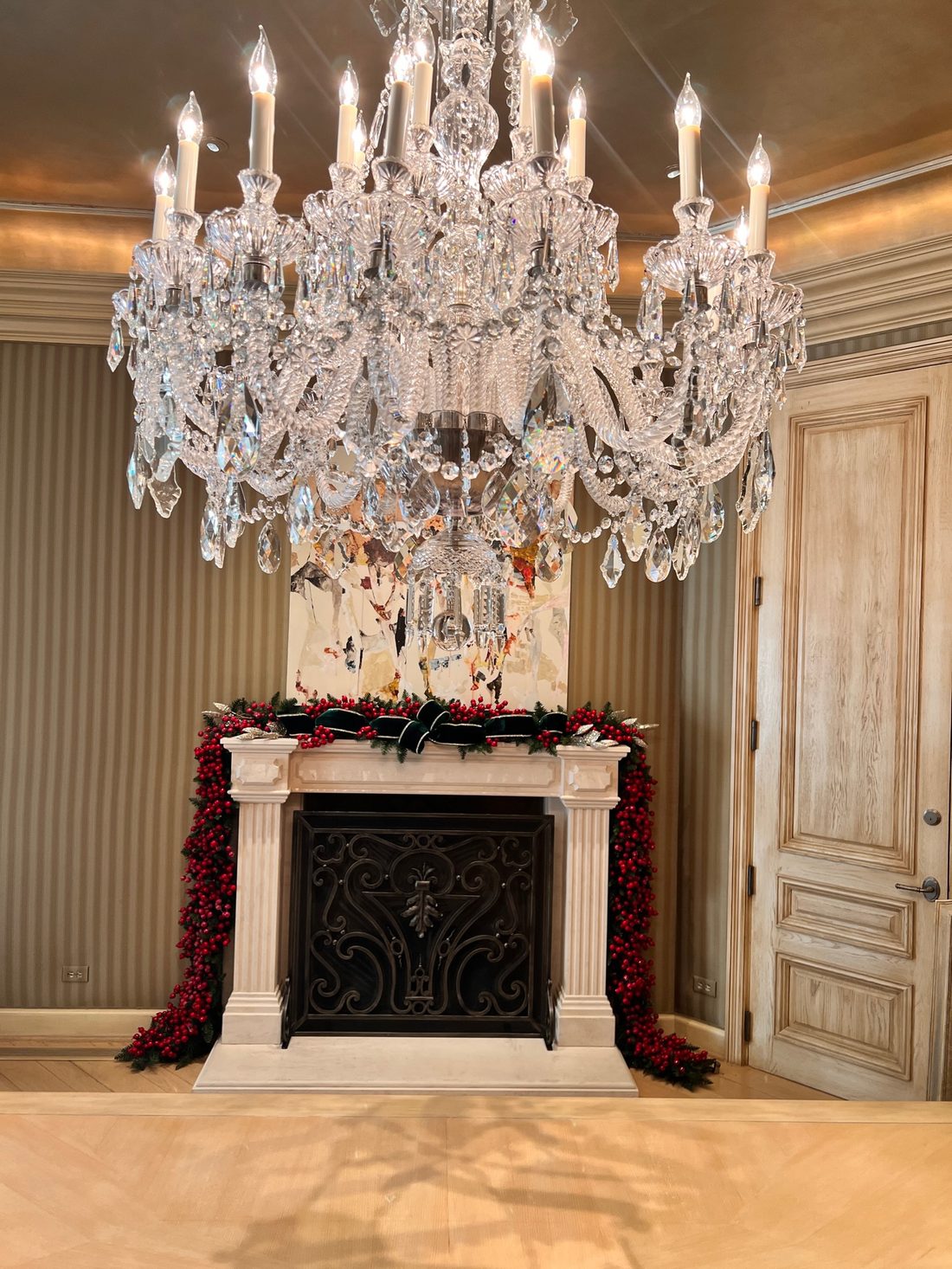 A crystal chandelier over a mantel with red garland