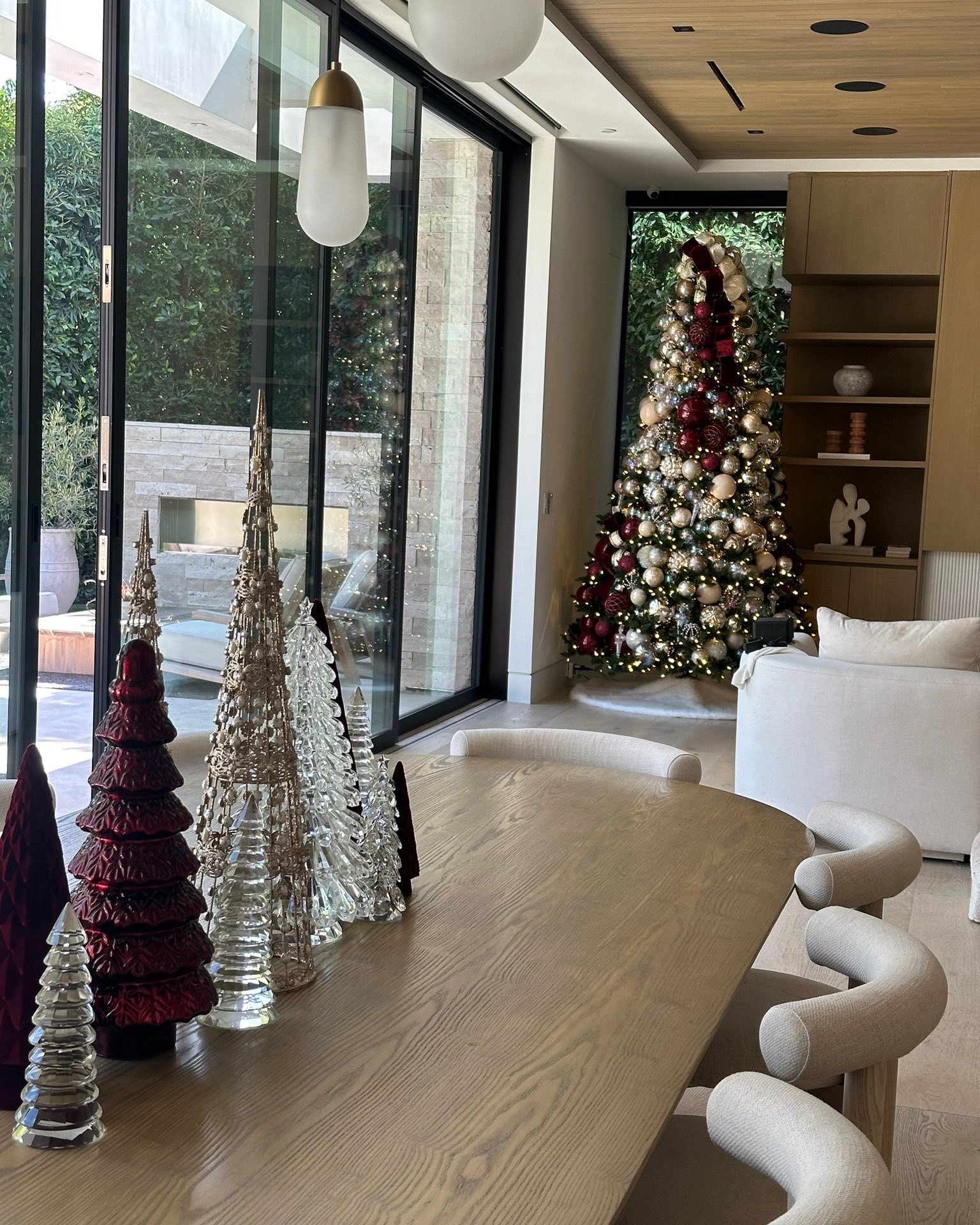 Glass and beaded tabletop trees on a dining table with a red and gold tree beyond