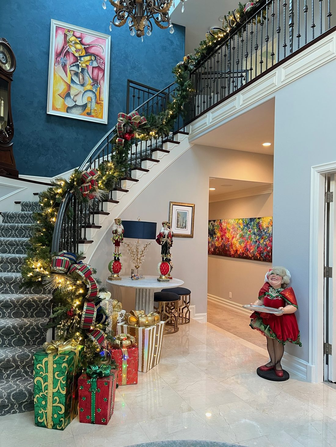 A two story foyer with garland along the curved stair and gifts below