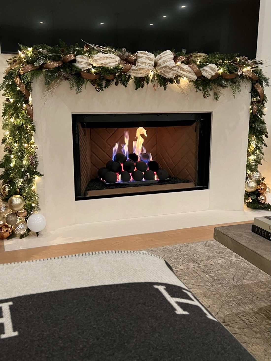 A lit fireplace with fresh garland and cream ribbon