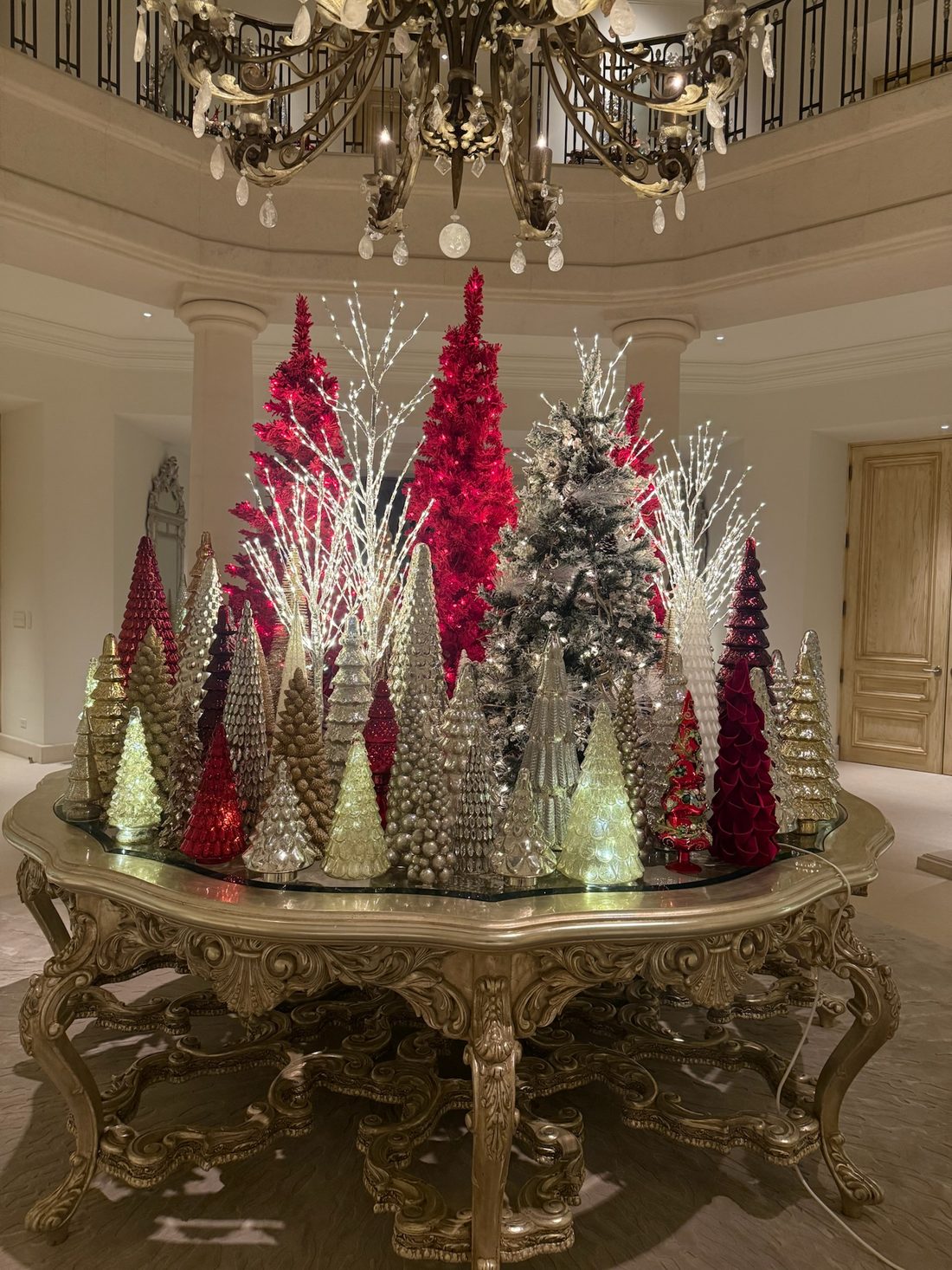A tabletop of pink, silver and white trees under a chandelier